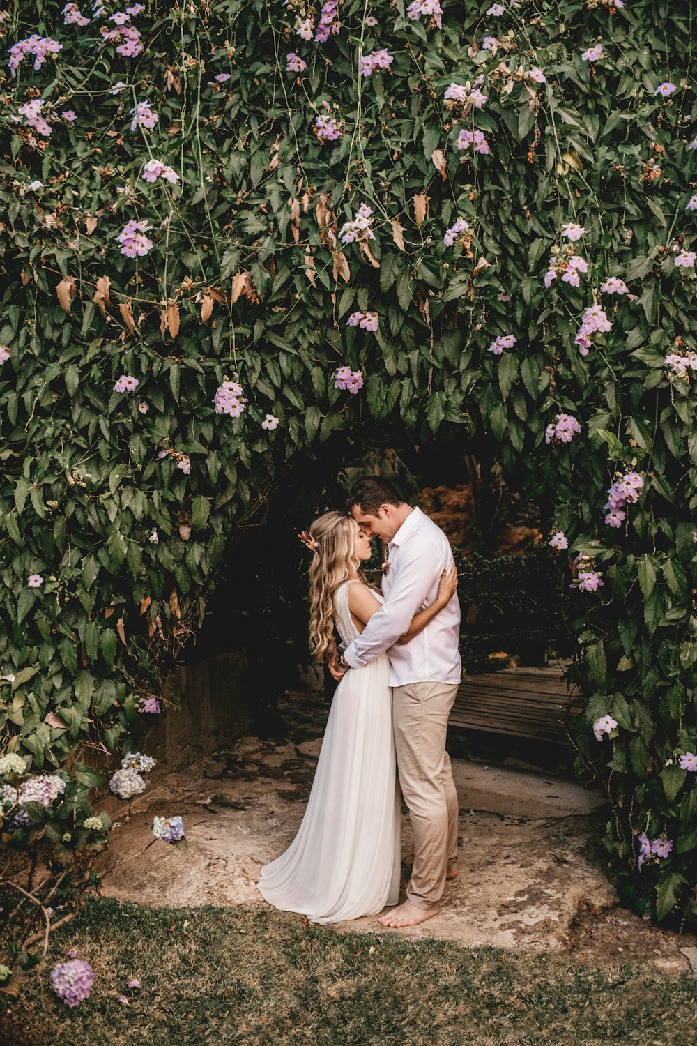 a bride and groom kissing in front of a wall of flowers