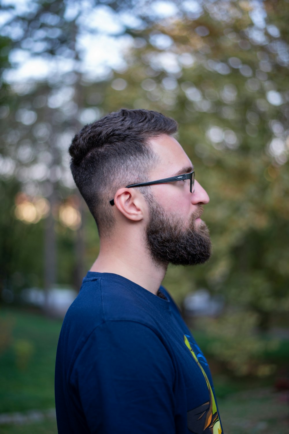 a man with a beard and glasses standing in a park