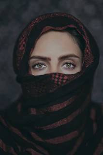 A close-up portrait of a young Iranian woman with a determined gaze, standing amidst a backdrop of peaceful protest.