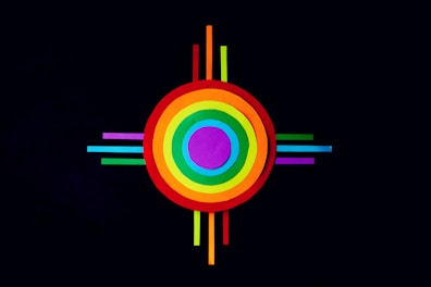 A colorful geometric design featuring concentric circles in various colors, including red, orange, yellow, green, blue, and purple. The circles are intersected by thin, equally spaced lines extending outward on all four sides against a black background.