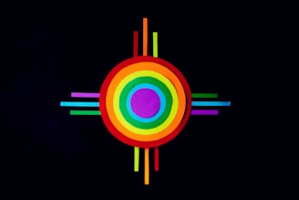 A colorful geometric design featuring concentric circles in various colors, including red, orange, yellow, green, blue, and purple. The circles are intersected by thin, equally spaced lines extending outward on all four sides against a black background.