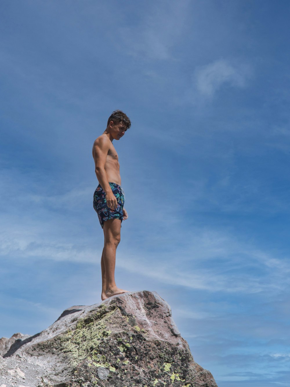 a young man standing on top of a large rock