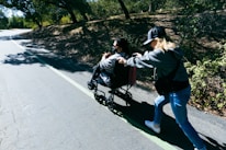A caring nurse helping a person with a disability enjoy a community outing on a sunny day.