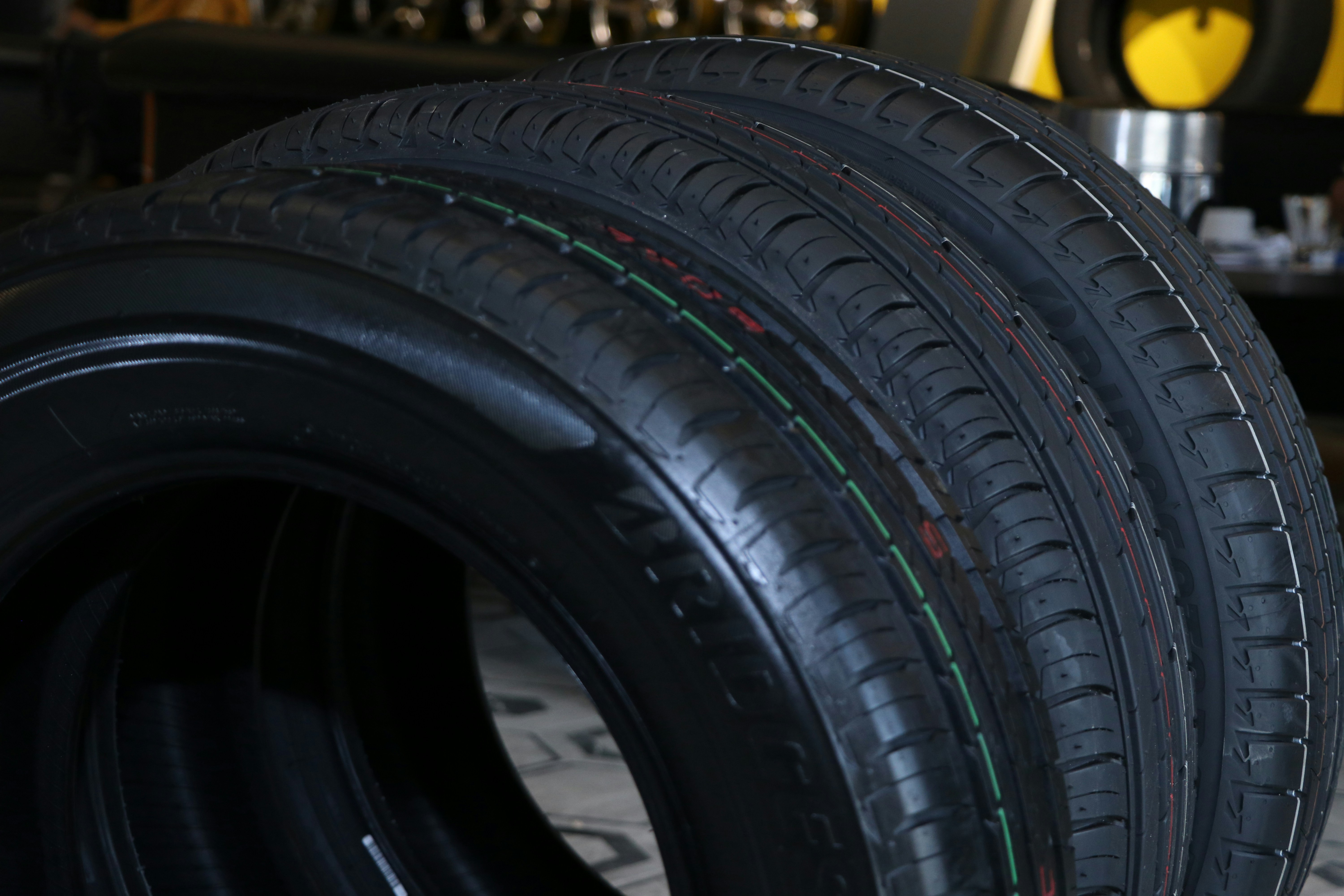 Row of new tires stacked neatly in a tire shop with dark background, showing tread patterns and sidewall details