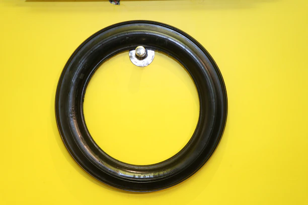 A black circular rubber tire is mounted on a vibrant yellow wall. The tire is centered and appears to be hung by a small metallic hook protruding from the wall.