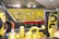 A modern showroom displaying various tires arranged neatly. The background features a bar-like area with red stools and a yellow accent wall. Tire racks display differently wrapped tires against a contrasting black and yellow theme. The lighting is bright, enhancing the contemporary design.