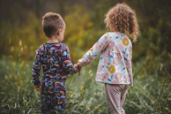 two children holding hands in a field of tall grass