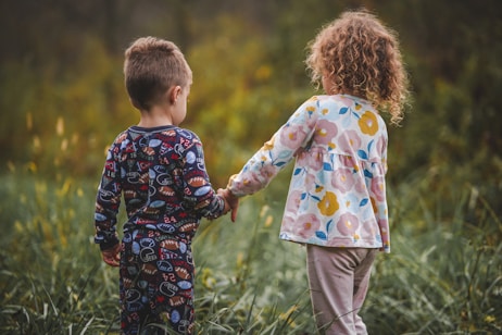 two children holding hands in a field of tall grass