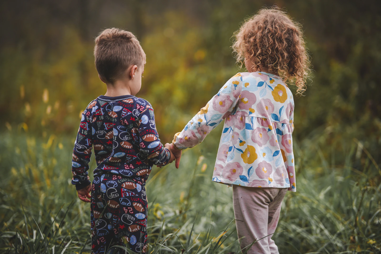 Dos niños tomados de la mano, vistos de espaldas, en un campo verde