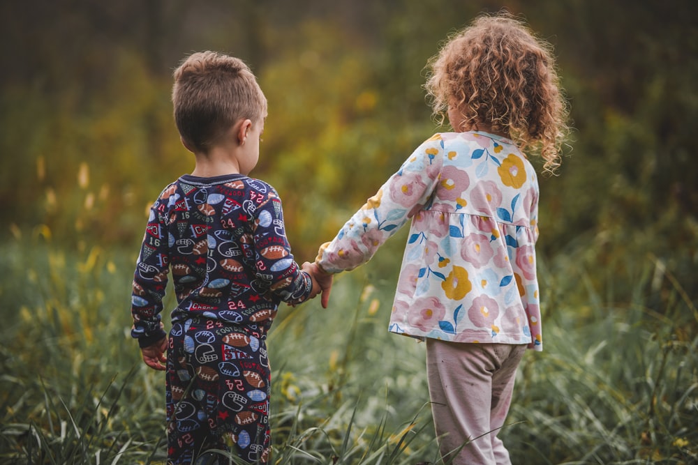 two children holding hands in a field of tall grass