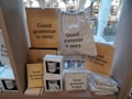 A display features various items like notebooks, mugs, a drawstring bag, and pouches, all with the phrase 'Good grammar is sexy.' The setting appears to be a store with books visible in the background.