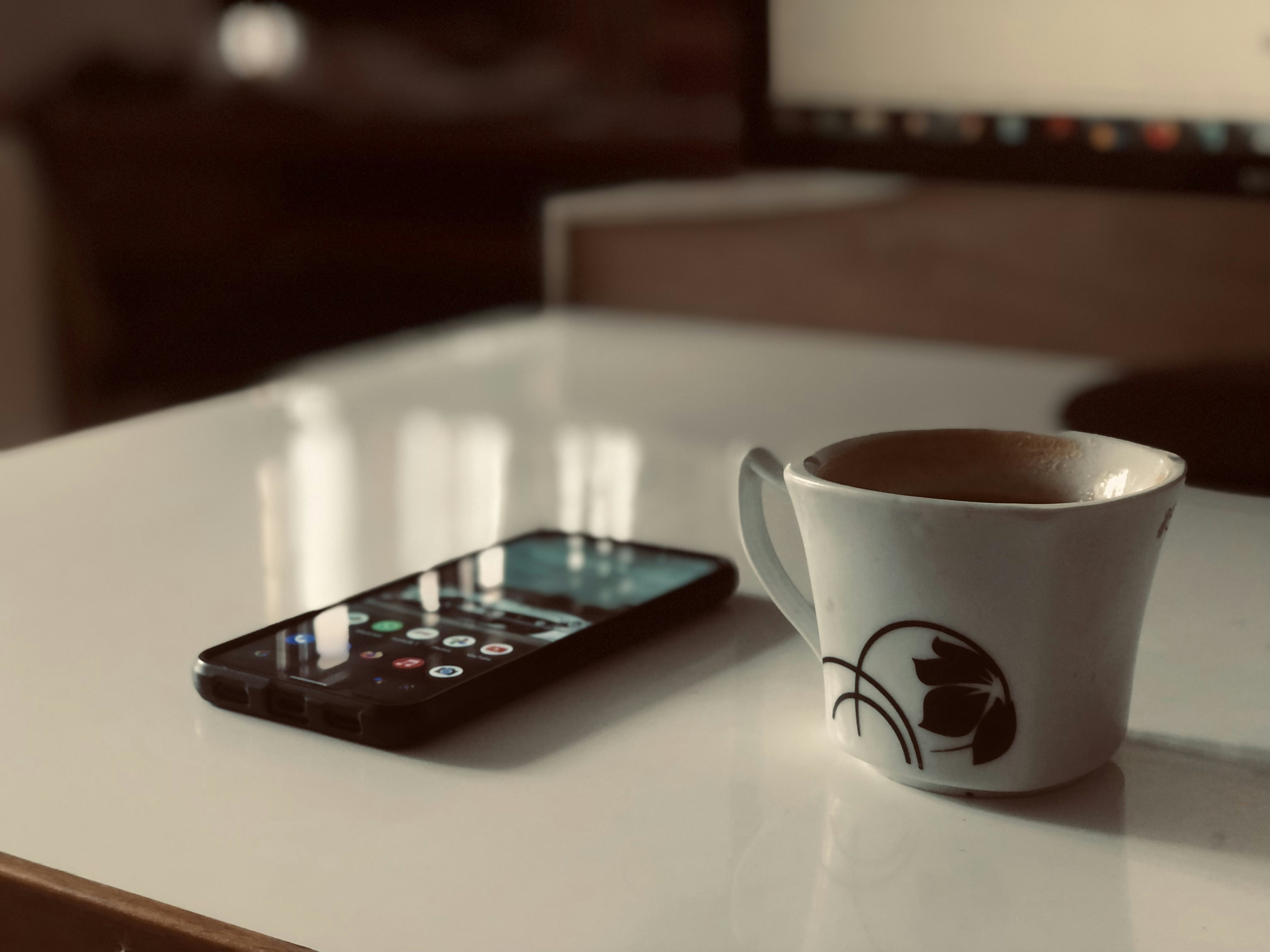 secangkir kopi di sebelah ponsel di atas meja