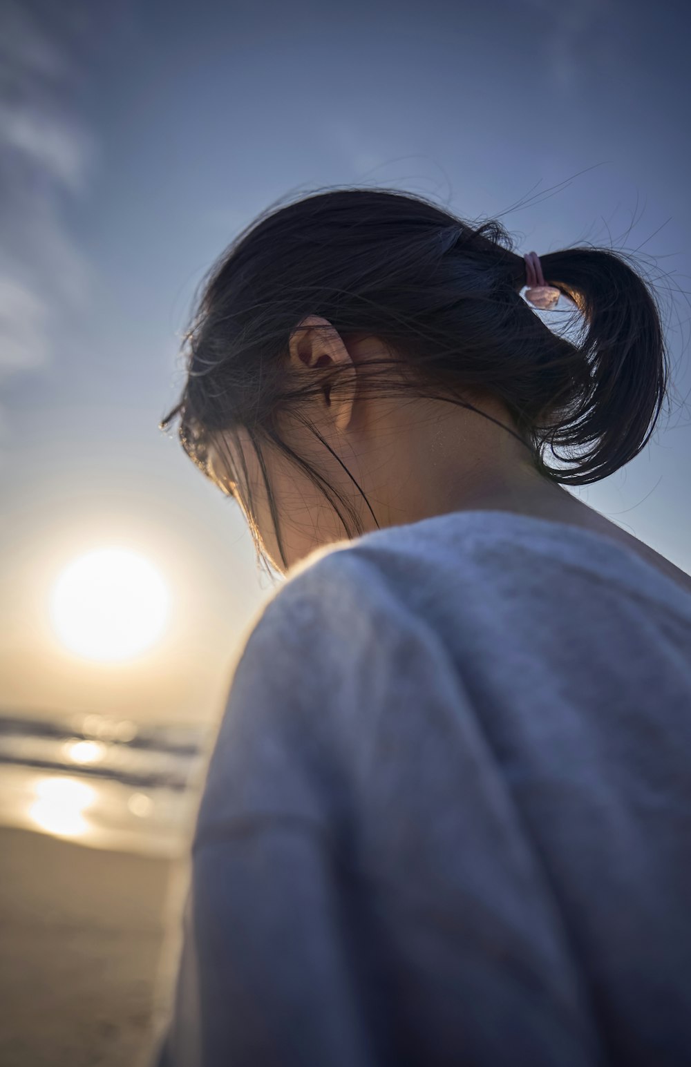 a woman standing on a beach with the sun in the background