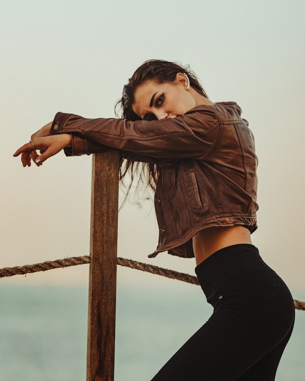 a woman leaning on a wooden post near the ocean