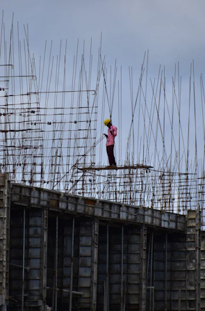 A confident engineer in a safety helmet reviewing blueprints beside iron rods