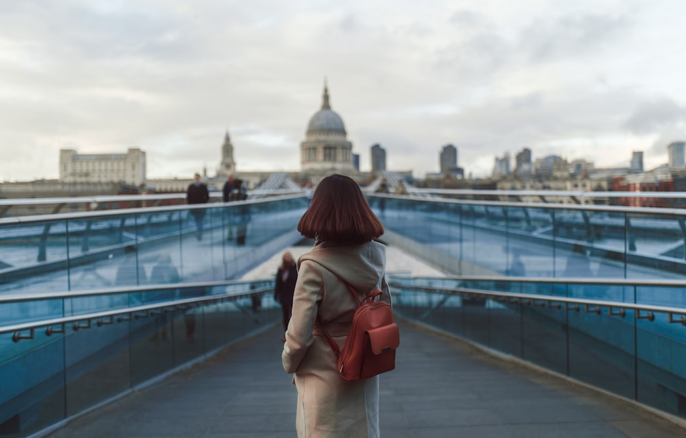 a woman walking across a bridge with a red purse