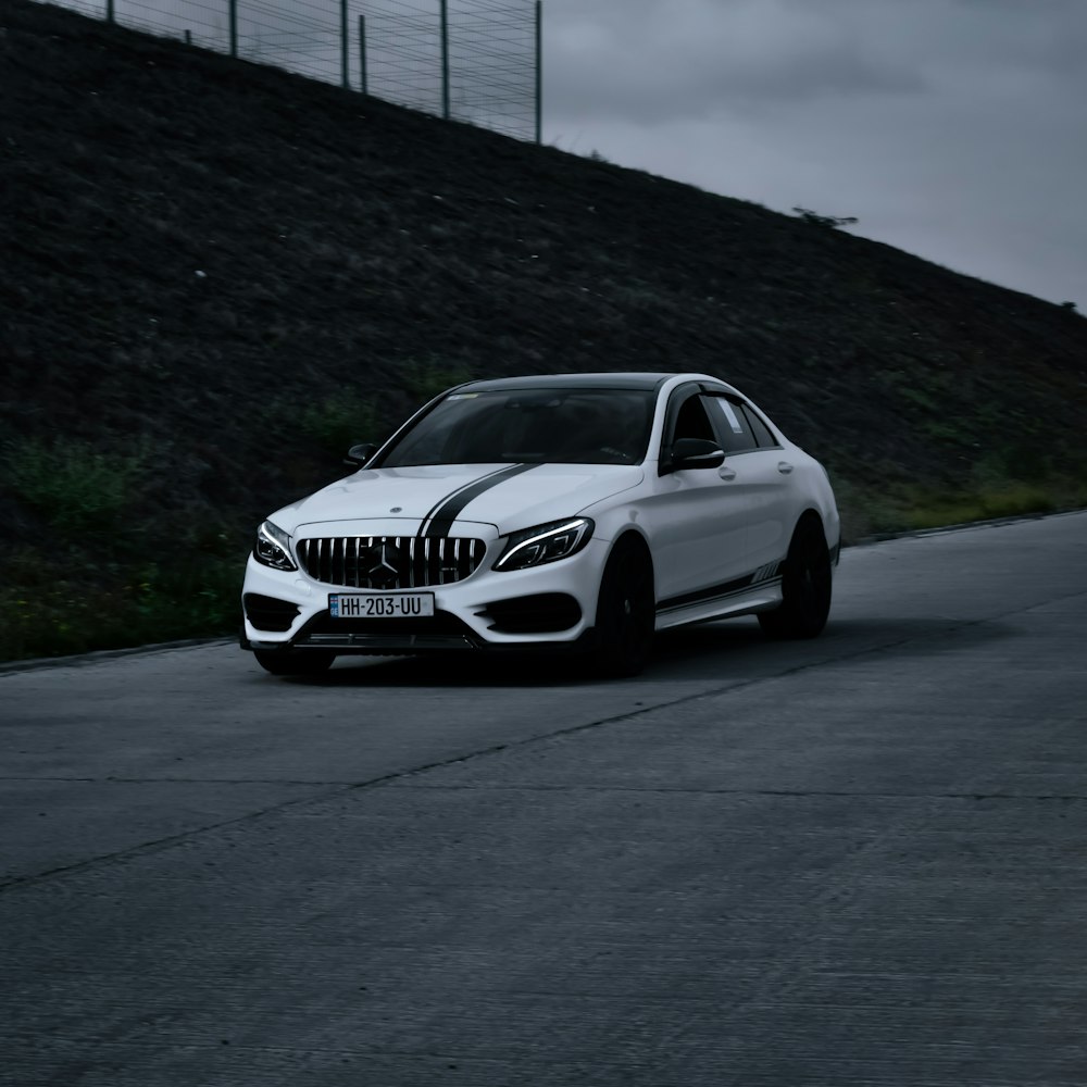 a white car driving down a road next to a hill