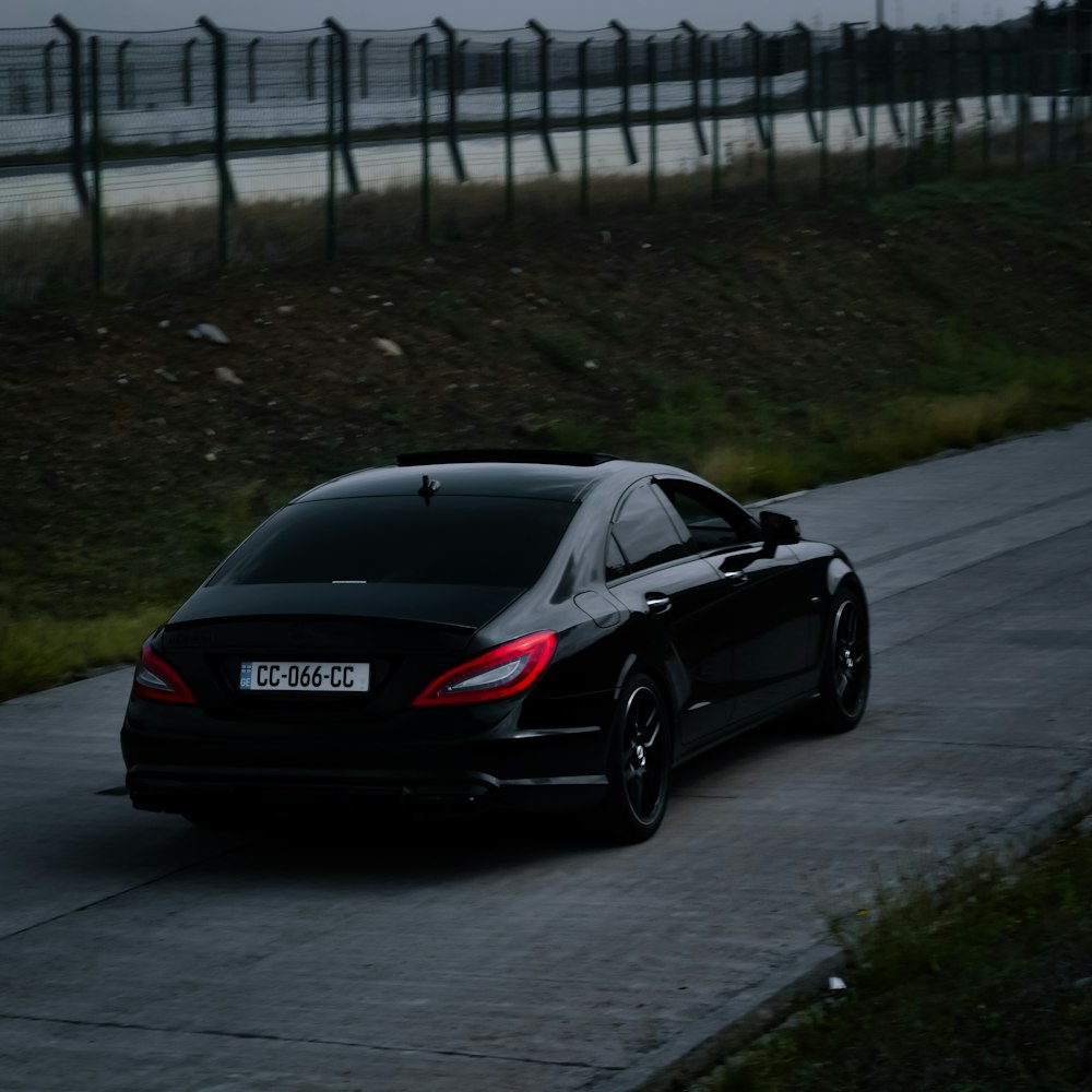 a black car driving down a road next to a fence