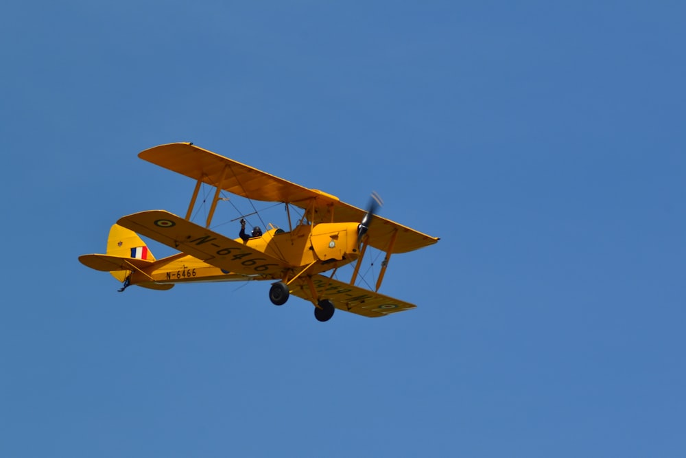 a small yellow airplane flying through a blue sky