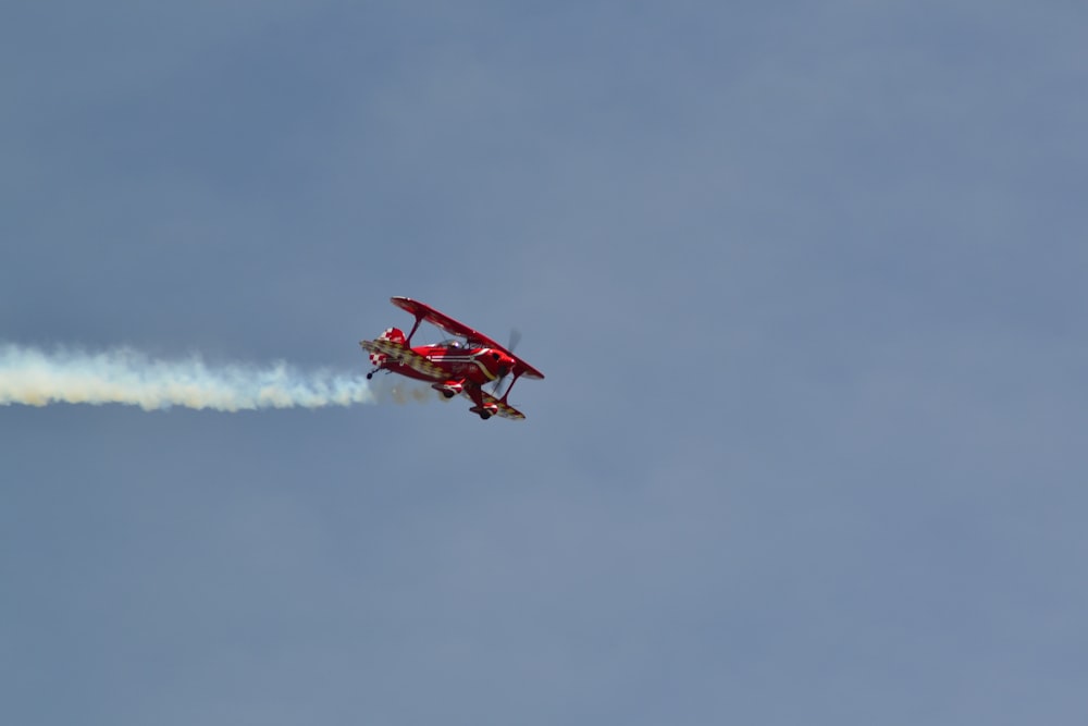 a small red plane flying through a blue sky