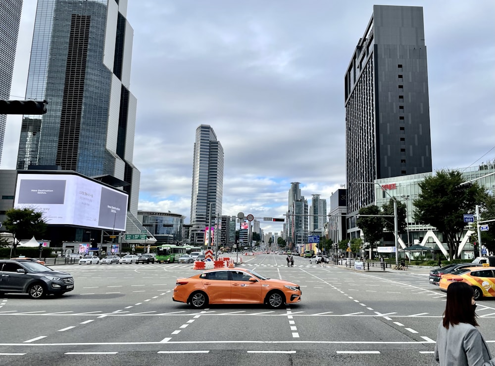 an orange car driving down a street next to tall buildings