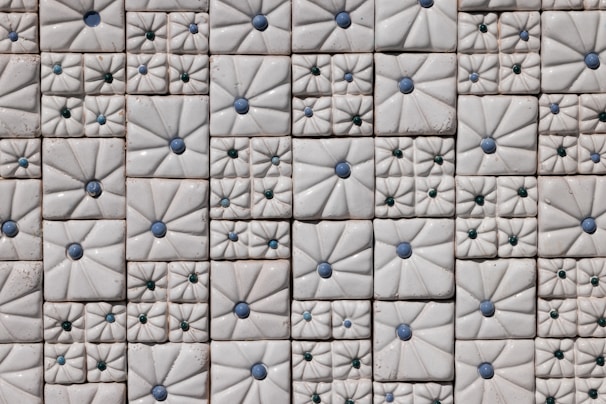 An arrangement of decorative ceramic tiles with raised designs, featuring blue and green circular accents. The tiles are mostly square-shaped and have intricate floral patterns that create a sense of texture and depth.