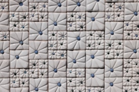 An arrangement of decorative ceramic tiles with raised designs, featuring blue and green circular accents. The tiles are mostly square-shaped and have intricate floral patterns that create a sense of texture and depth.