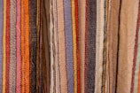Colorful woven textiles with vertical stripes in various shades including blue, red, yellow, orange, black, and beige. The fabric appears to have a textured surface, typical of traditional woven materials.