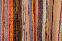 Colorful woven textiles with vertical stripes in various shades including blue, red, yellow, orange, black, and beige. The fabric appears to have a textured surface, typical of traditional woven materials.