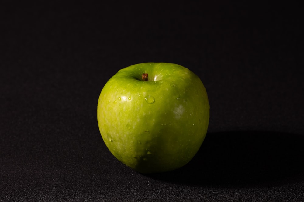 a green apple sitting on top of a black table