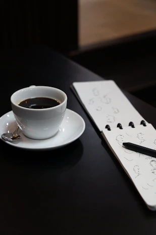 A cheerful mug filled with coffee, sitting on a desk beside a sketchbook and colorful pens.