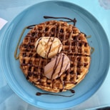 a blue plate topped with a waffle covered in chocolate