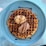 A large, round waffle sits on a blue plate, topped with two scoops of ice cream—one vanilla and one chocolate. The waffle is drizzled with chocolate and caramel sauce, creating a rich, indulgent look.