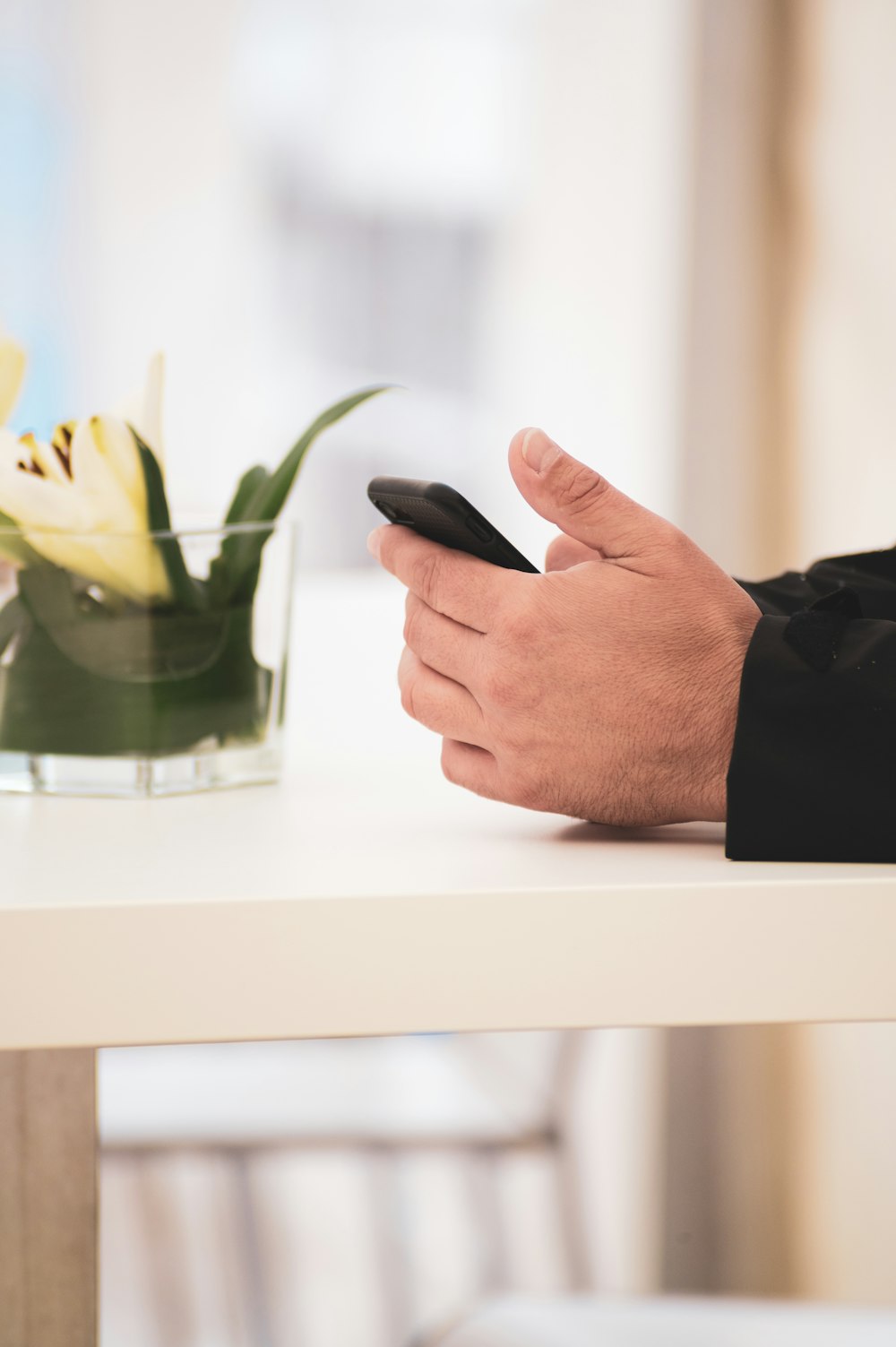 a man holding a cell phone next to a vase of flowers