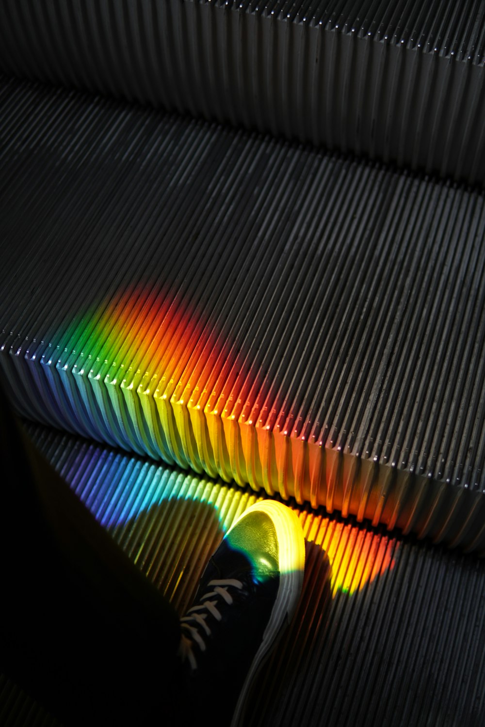 a person's shadow on an escalator with a rainbow light coming from