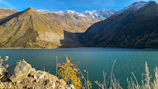 A serene Qinghai lake reflecting the colorful autumn foliage and distant snow-capped peaks.