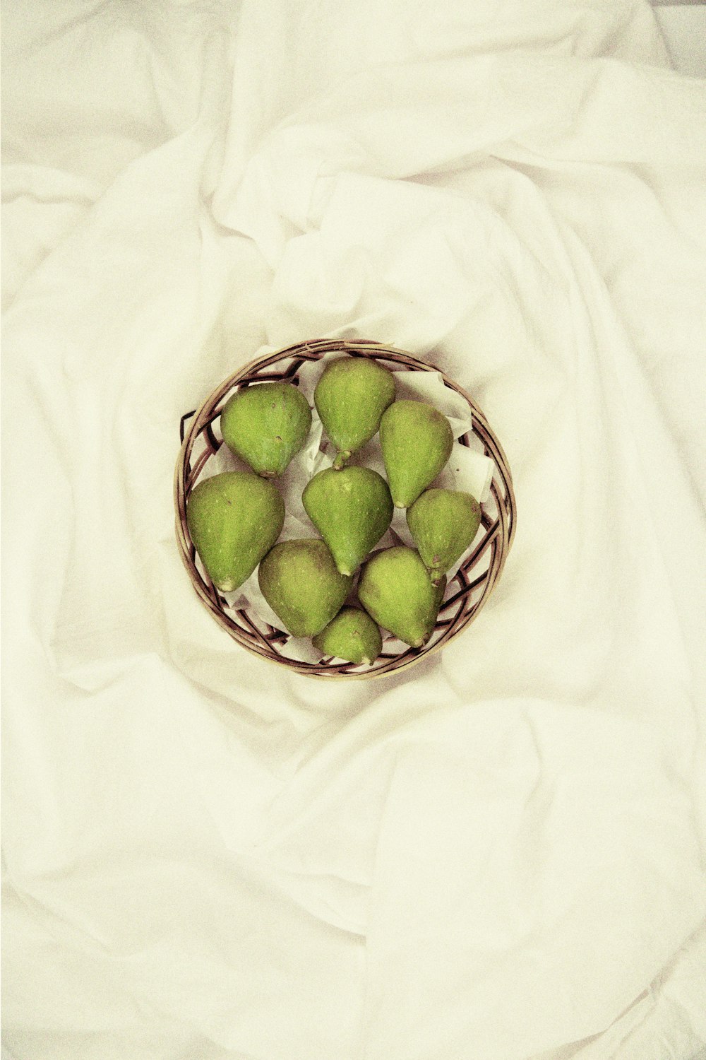 a basket filled with green apples on top of a white sheet