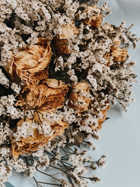 A delicate arrangement of muted dried flowers in soft pastel tones resting on a rustic wooden table.