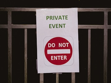A sign is attached to a metal railing. The sign reads 'PRIVATE EVENT' in green text and features a red circle with a white horizontal bar accompanied by the words 'DO NOT ENTER' in white.