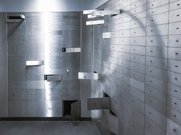 A room filled with numerous metallic safety deposit boxes, many of which are open, creating an intriguing and mysterious atmosphere. The boxes are arranged in neat rows along the wall, and the lighting casts subtle shadows.
