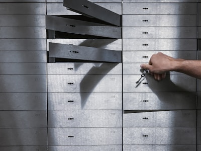 A hand holding a set of keys is reaching to open a series of safety deposit boxes. Some boxes are open, and the keyholes are visible. The boxes are metallic, numbered, and arranged in an organized manner.