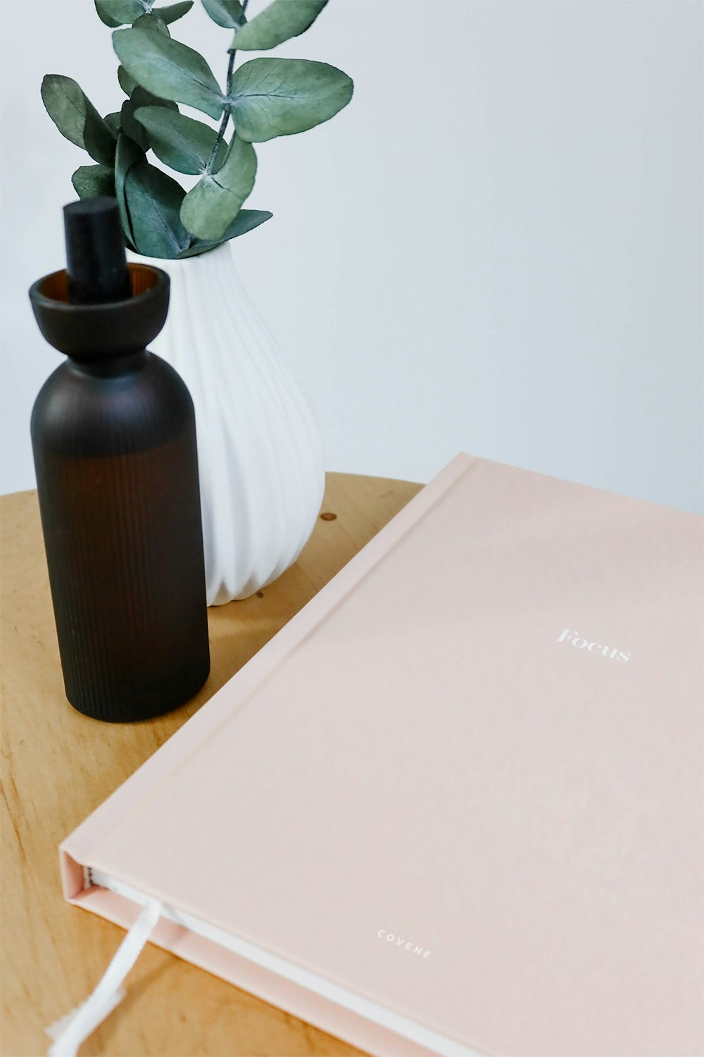a white vase with a green plant next to a pink notebook