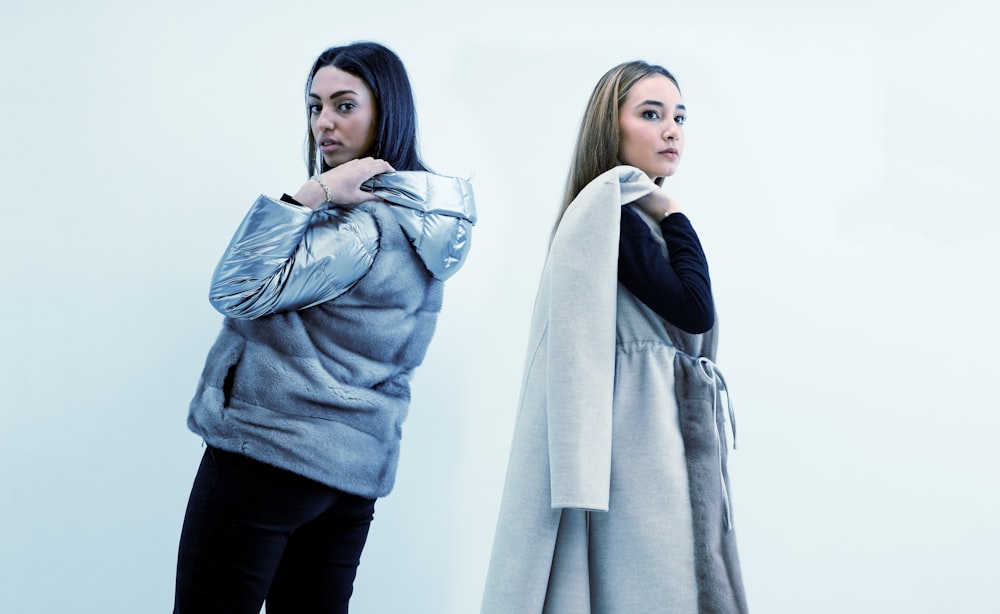 two women standing next to each other in front of a white wall