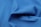 A close-up of a blue fabric with visible texture and folds, showcasing the knit pattern and the soft drape of the material.