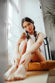 Bright, airy shot of a smiling woman practicing gentle face yoga by a sunlit window.