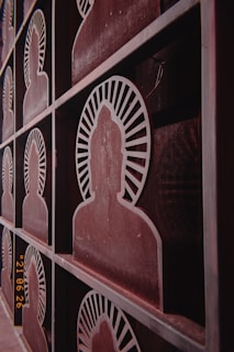 Metallic panels are designed with cut-out silhouettes of seated figures, likely representing a meditative or spiritual theme. Each silhouette is encircled by a radiating pattern, resembling rays, and arranged in a grid-like structure. The surface shows a weathered, rusty finish with a vintage aesthetic.