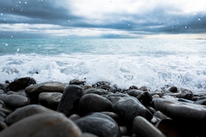 A slow-motion video still of waves crashing on a rocky shore under a cloudy sky