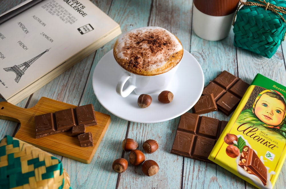 a cappuccino, chocolate, and a book on a table