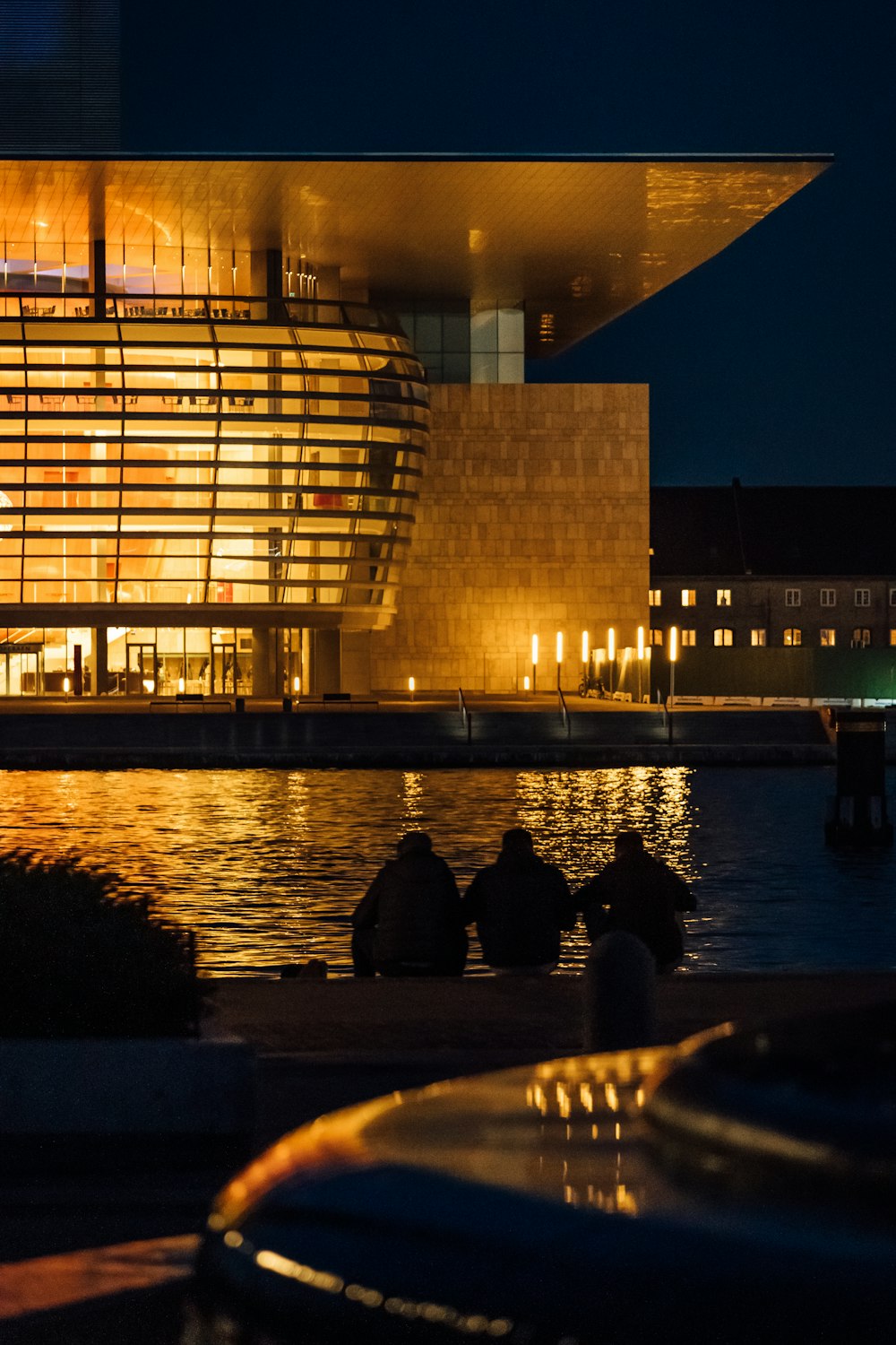 people are sitting on the edge of a body of water in front of a building