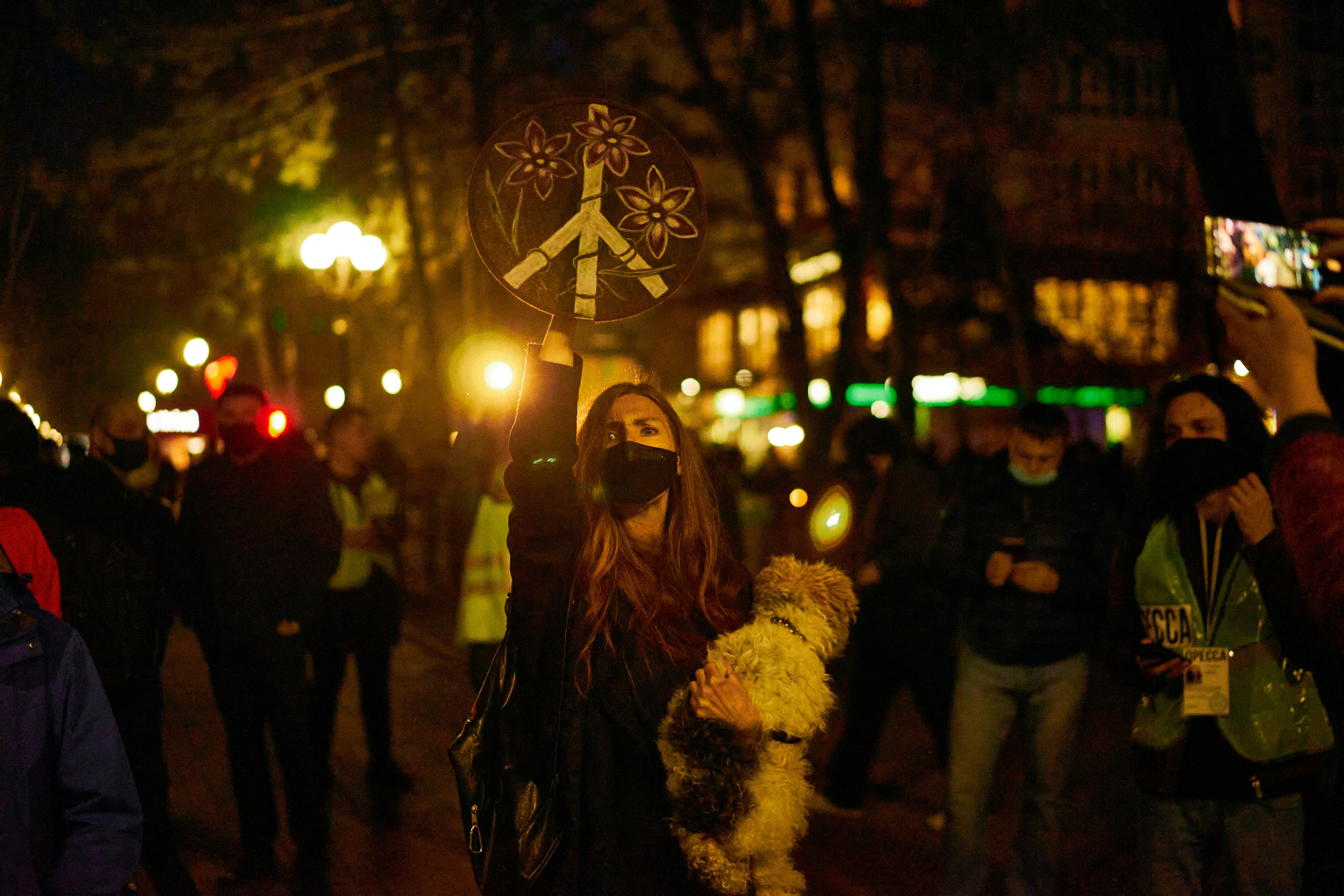 A girl holding a peace sign with one hand and a dog with the other at a rally in support of Alexei Navalny. 